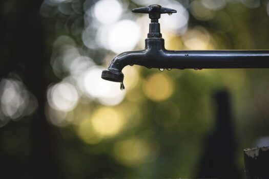 A glass of clear tap water with a water filter pitcher in the background, symbolizing water purification and safety.