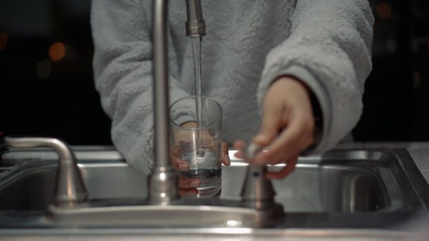 A clear water filter system installed in a kitchen, with a glass of clean water beside it, showcasing the importance of water purification.
