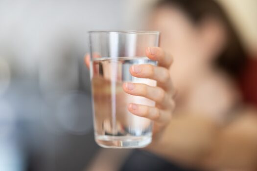 A glass of clear, refreshing water with a slice of lemon and mint leaves, placed on a wooden table.